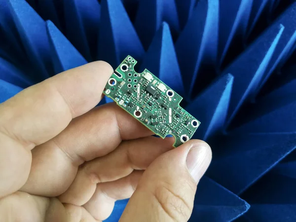 Electronics engineer hand holding printed circuit board in front of radio frequency absorbers