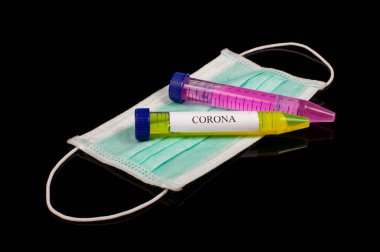 Test tüpünde parlak sarı sıvılar ve siyah yansıtıcı arka planda izole edilmiş CORONA yazılı yüz maskesi. Corona COVID-19 virüs konsepti.