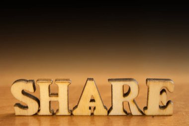 Kelime 'share' ahşap harflerin yapılmış. Tablo ve koyu siyah arka plan üzerinde ahşap yazıt