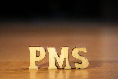 Kelime 'pms' ahşap harflerin yapılmış. Tablo ve koyu siyah arka plan üzerinde ahşap yazıt