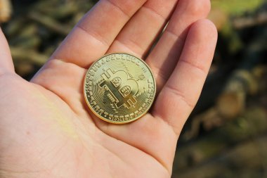 Altın bir Bitcoin açık bir yüzeyde yatıyor. Para parlar ve ışığı yansıtır. Arka plan karanlık ve soyut.