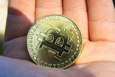 Altın bir Bitcoin açık bir yüzeyde yatıyor. Para parlar ve ışığı yansıtır. Arka plan karanlık ve soyut.