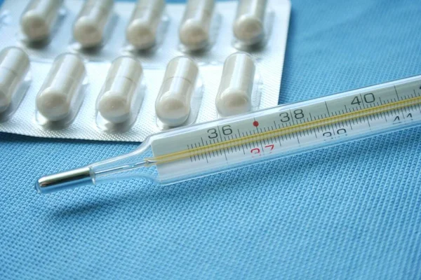 Tablets, pills and mercury thermometer on a blue background. Flu cold concept. Healthcare medical concept. Medicine pill. Emergency medical treatment.