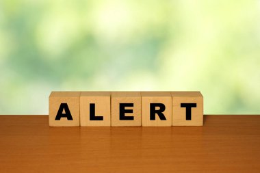 Küp bloklardaki ahşap bir masada yeşil bir doğa grubuyla ALERT mesajı.