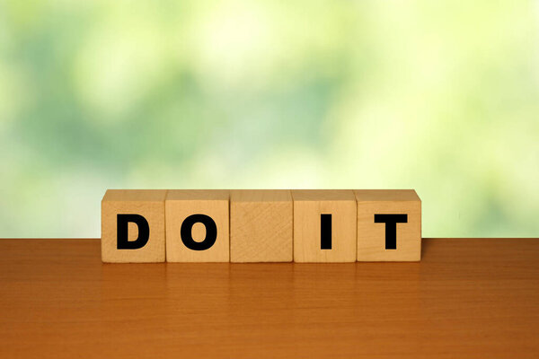 Do IT message word on a wooden desk on cube blocks with a green nature backgroun
