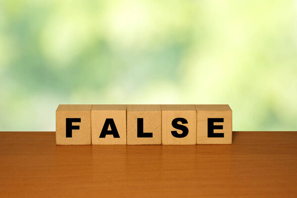 FALSE message word on a wooden desk on cube blocks with a green nature backgroun