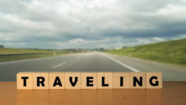 TRAVELING message word on a wooden desk on cube blocks with a empty road backgroun