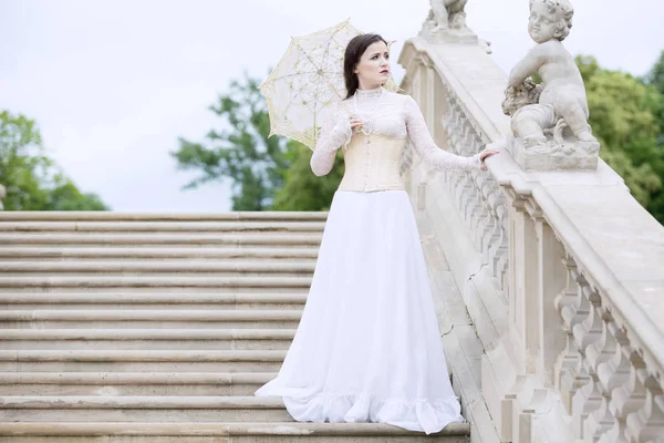 Frau im weißen viktorianischen Kleid mit Regenschirm auf der Treppe — Stockfoto