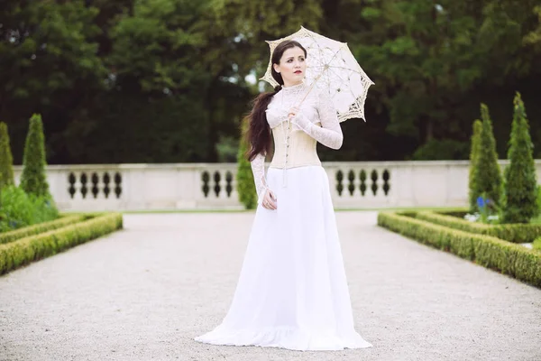 Kvinna i vit viktoriansk klänning med paraply i park — Stockfoto