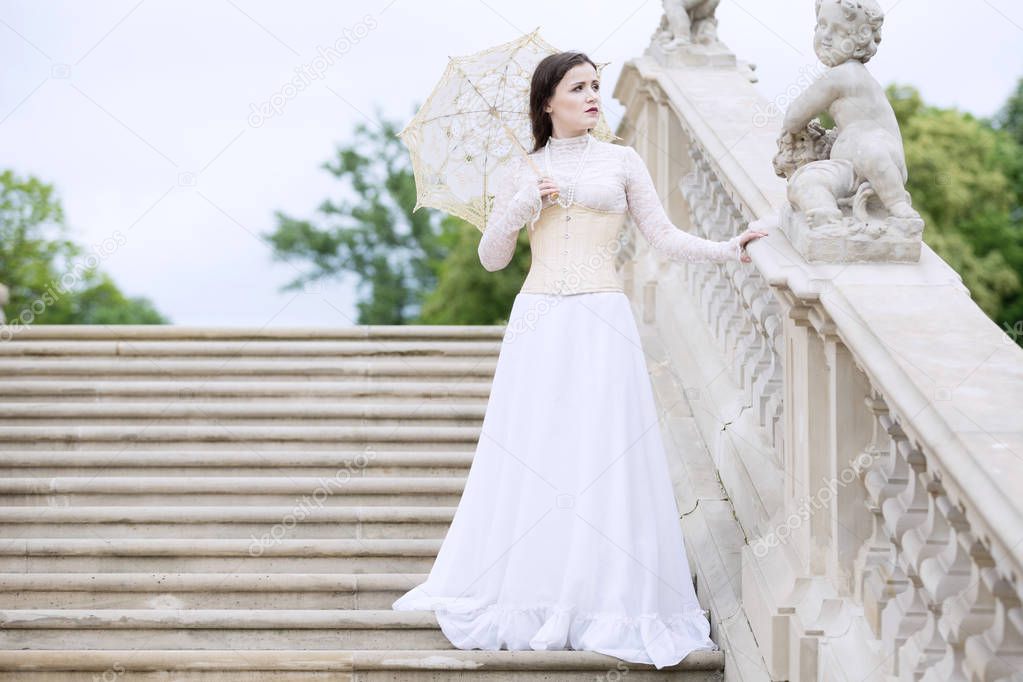 Woman in white Victorian dress with umbrella on stairs