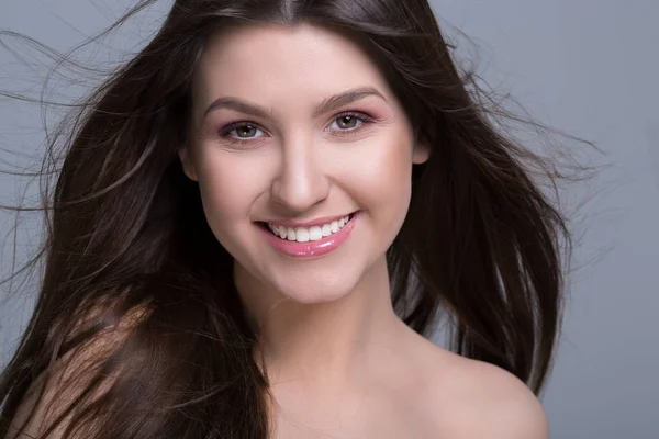 Vackra leende kvinna med långt hår på en grå bakgrund — Stockfoto