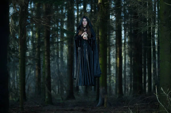 Bruxa com um crânio levitando na floresta — Fotografia de Stock