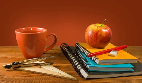 Канцелярские принадлежности, чашка и яблоко на деревянном столе — стоковое фото