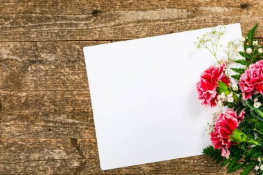 Eski Ahşap Arkaplan 'daki karanfil çiçeklerinin kağıt yaprağıyla üst görüntüsü. Anneler günü için tasarım konsepti, düğün ve fotokopi odalı sevgililer günü. Seçici odak.