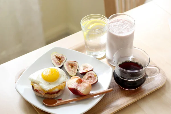 Egg muffin with fig, coffee, milk and lemon water on a wooden try