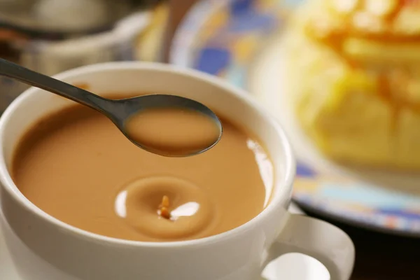Una gota de té en un té de leche caliente con cuchara — Foto de Stock