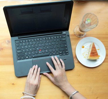 Bir peynir pasta ve bir ahşap bir içki ile laptop yazarak kız