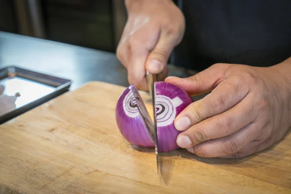 Chef hacher un oignon rouge avec un couteau sur la planche à découper Photo De Stock