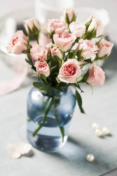 Pink spray roses in blue vase on grey background