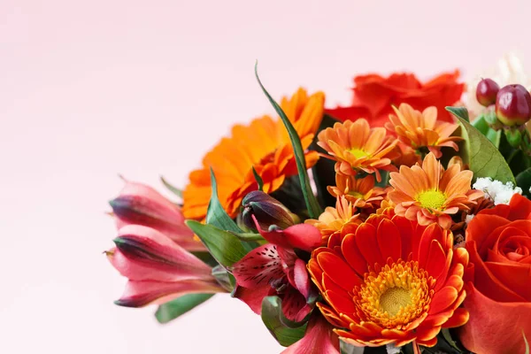 Mixed bouquet of red and orange flowers on pink background