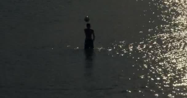 Barn som leker med en boll i havet vid solnedgången — Stockvideo