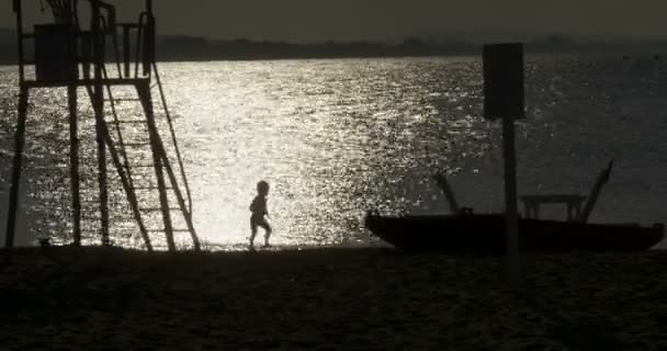Силуэт ребенка, играющего с песком на берегу моря — стоковое видео