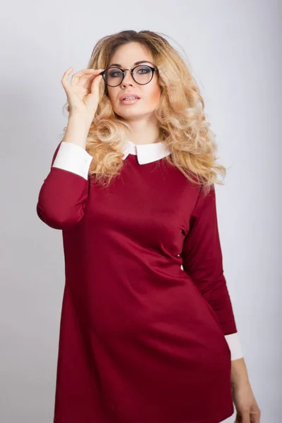 Ritratto di bella donna bionda caucasica con capelli ricci in piedi su sfondo grigio. Giovane donna d'affari con gli occhiali guardando la fotocamera — Foto Stock