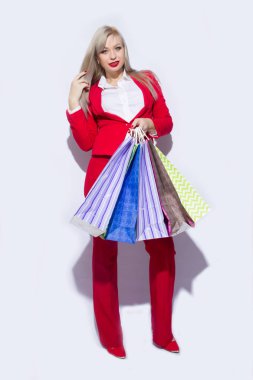 Genç sarışın Bayan alışveriş torbaları ile poz ve kamera için beyaz arka plan üzerinde seyir Kırmızı kostümlü resmini