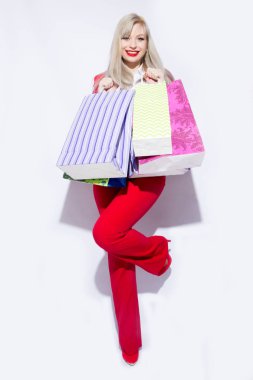 Genç sarışın Bayan alışveriş torbaları ile poz ve kamera için beyaz arka plan üzerinde seyir Kırmızı kostümlü resmini