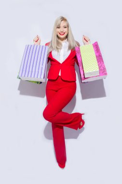 Genç sarışın Bayan alışveriş torbaları ile poz ve kamera için beyaz arka plan üzerinde seyir Kırmızı kostümlü resmini