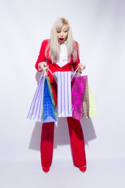 Genç sarışın Bayan alışveriş torbaları ile poz ve kamera için beyaz arka plan üzerinde seyir Kırmızı kostümlü resmini