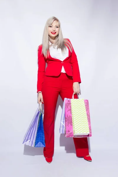 ショッピング バッグとポーズ カメラに肩越しに白い背景の赤い衣装で若い金髪女性の画像 — ストック写真