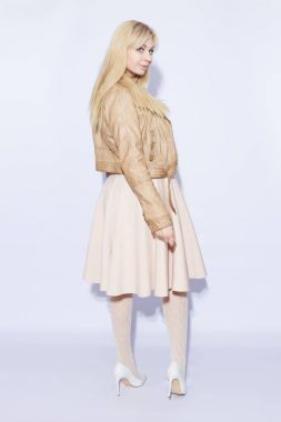 Trendy kahverengi ceketli poz ve photoshoot üzerinde gülümseyen kadın çarpıcı. Kapalı fotoğraf beyaz arka plan dalga uzun sarı saçlı güzel kız. İzole