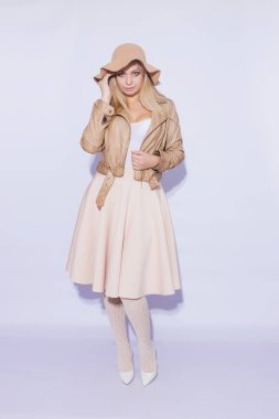 Tam uzunlukta portre güzel genç sarışın bir kadın. Kız MIDI bej etek ve kahverengi kısa ceket giymiş. Kafasına kahverengi şapka var. Bacaklar dantel çorap ve beyaz ayakkabı topuğu ile