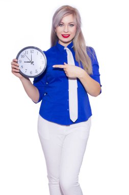 Stüdyo iş güzel bir sarışın genç kadın koyu mavi tişört, beyaz pantolon ve beyaz kravat portresi. Kız bir saat tutuyor. İzole. Kopya alanı