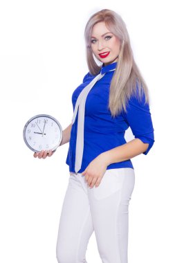 Stüdyo iş güzel bir sarışın genç kadın koyu mavi tişört, beyaz pantolon ve beyaz kravat portresi. Kız bir saat tutuyor. İzole. Kopya alanı