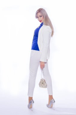 Beyaz pantolon takım uzun saçlı güzel bir genç sarışın kadının tam uzunlukta portre Studio. Bir kız yüksek topuklu Simli ayakkabı, o küçük gümüş el çantası elinde tutan