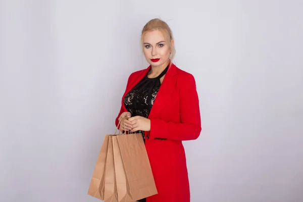 Imagem de mulher loira excitada em casaco vermelho segurando sacos de compras marrom isolado no terreno de panificação branco — Fotografia de Stock