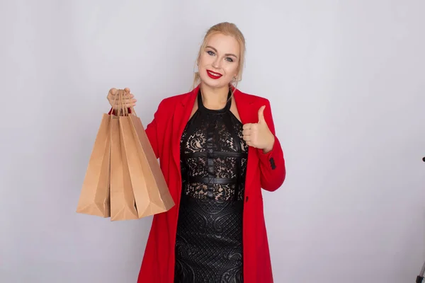 Afbeelding van opgewonden blonde vrouw in rode jas met bruine boodschappentassen geïsoleerd op witte bakcground — Stockfoto