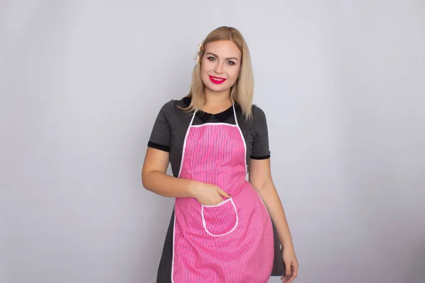 Mujer rubia en vestido gris con cocina blanca y delantal ppink — Foto de Stock