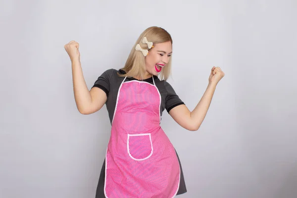 Blondýny žena v šedých šatech na sobě kuchyně bílá a růžová zástěra — Stock fotografie
