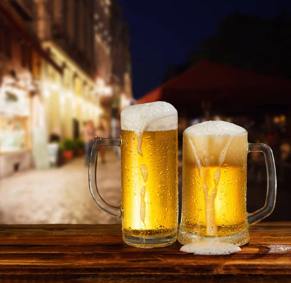 街の背景に泡とビールの冷たいマグカップ — ストック写真