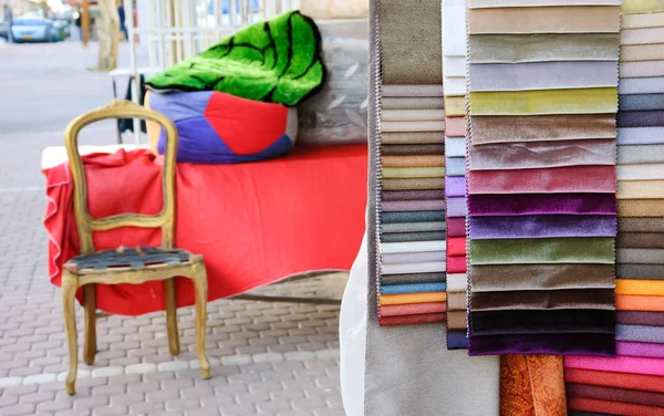 Colorful upholstery samples and wooden frame of  antique armchair near the entry to the workshop. Beersheba, Israel. Selective focus on the upholstery samples.