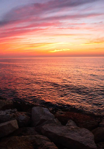 Gyönyörű arany naplemente a tengeren, telített ég és a felhők. Tükörképét a vízben. Sziklás part menti vonal. Békés nyugodt táj. Természet háttér. — Stock Fotó