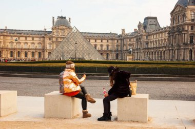 Paris, Fransa - 14 Ocak 2018: Louvre Müzesi yakınlarında genç şık bayan turistler dinleniyor, mesajlaşıyor, telefonla konuşuyor. Sosyal medya bağımlılığı kavramı. 