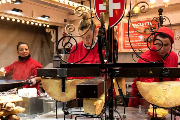 PARIS, FRANCE - JANUARY 6, 2019:  Young woman preparing hot melted Raclette cheese sandwich at traditional Savoie food stall at Christmas market in Tuileries Garden. — Stock Photo, Image