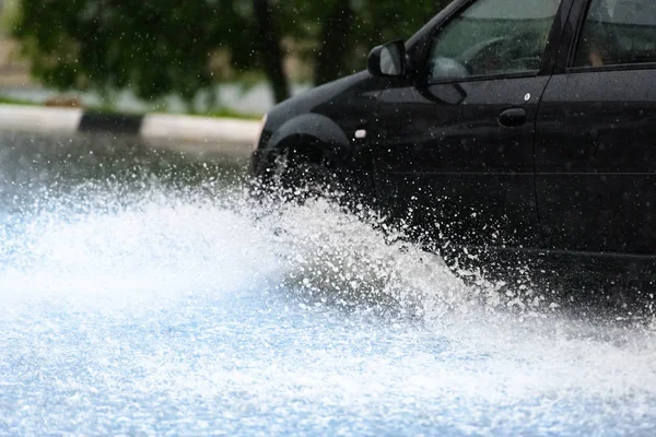 Araba yağmuru su sıçratıyor.