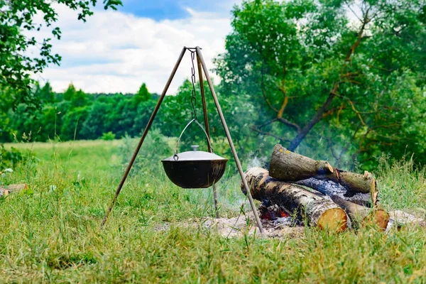 A camp-steaky sooty food bowl hanging on a tripod over a fire — Stock Photo, Image