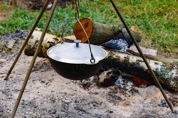 A camp-steaky sooty food bowl hanging on a tripod over a fire — Stock Photo, Image