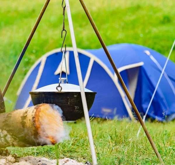 A camp-steaky sooty food bowl hanging on a tripod over a fire — Stock Photo, Image